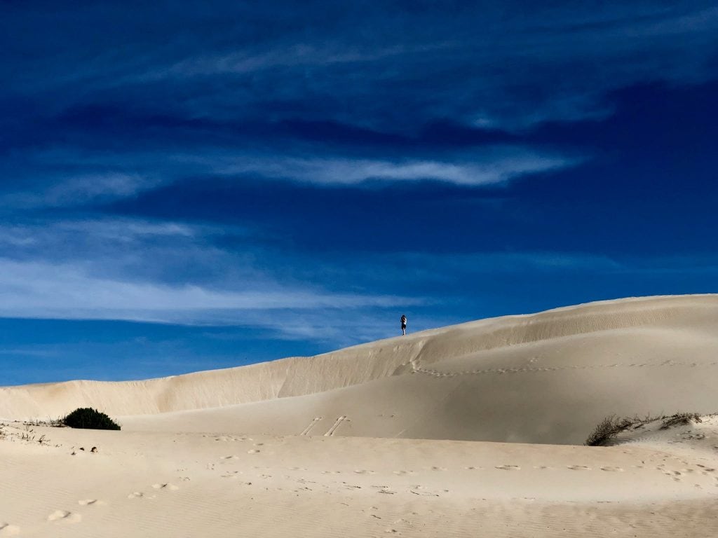 Lone figure standing on sandhills with ocean behind