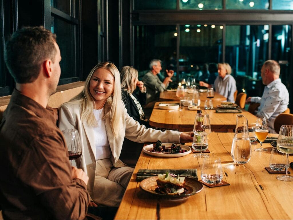 Group Dining at a long table enjoying food and drinks in a modern ocean-to-table restaurant.