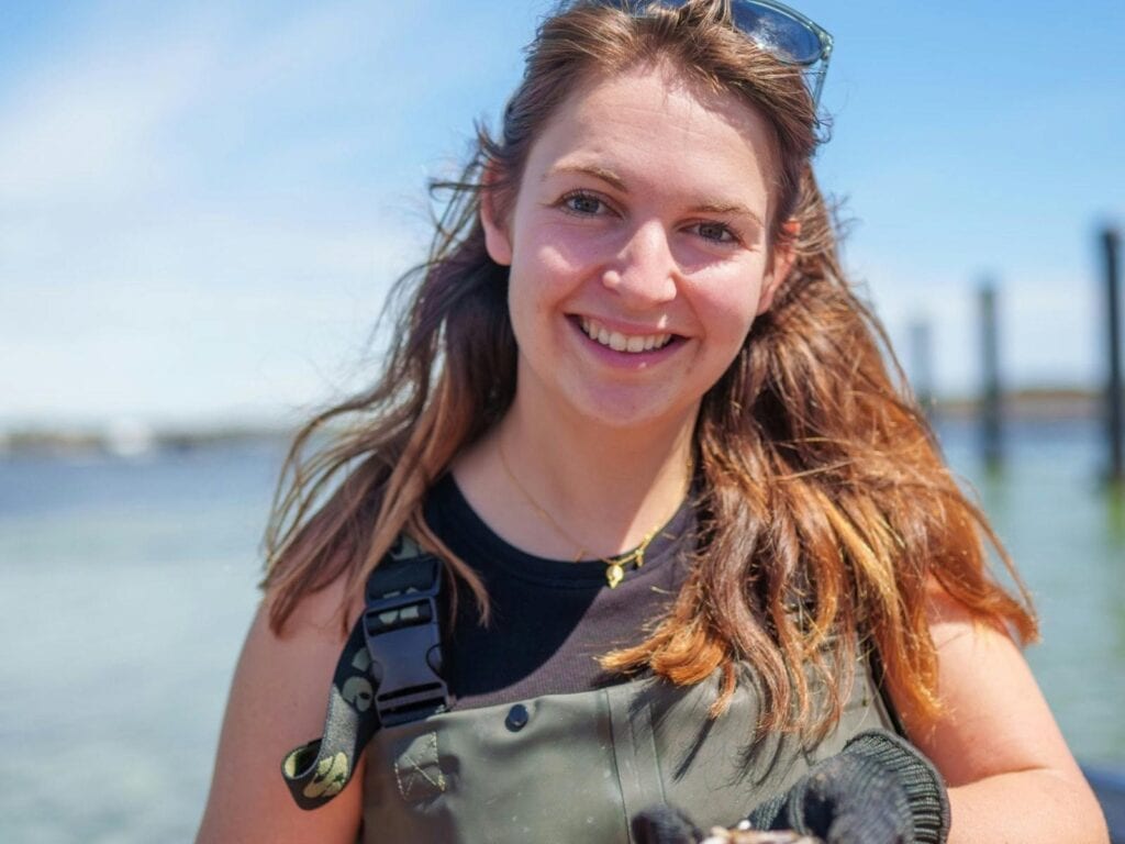 Woman in waders holding a fresh oyster during a Coffin Bay oyster farm tour, South Australia