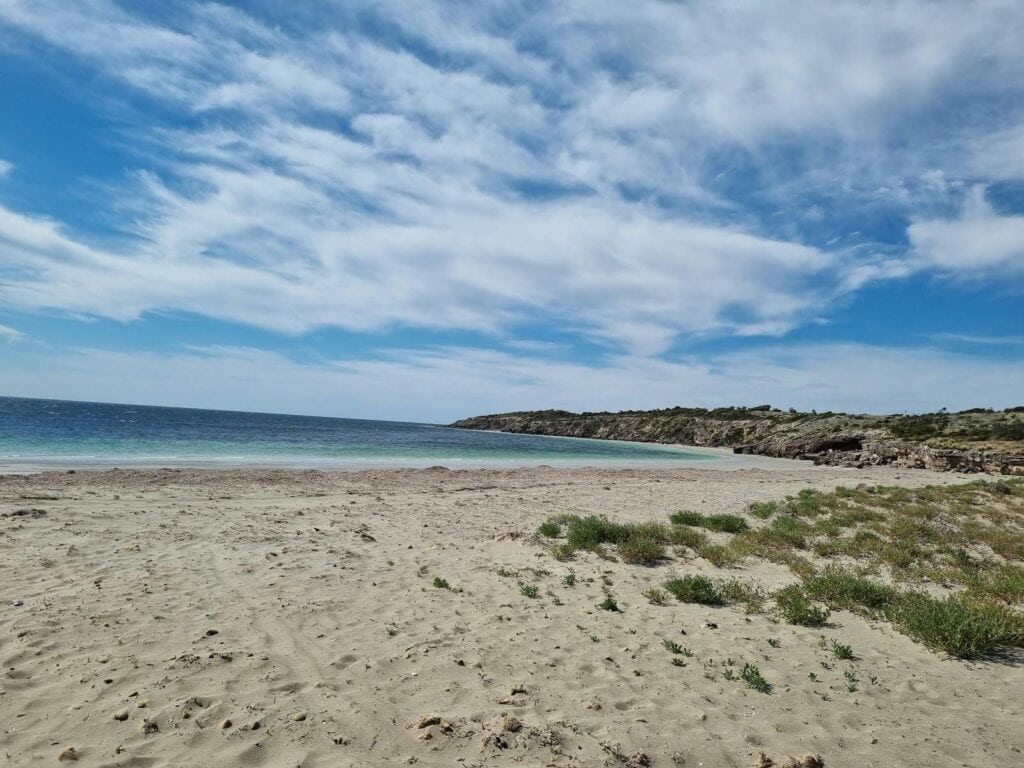 Wide sandy shoreline at Farm Beach under sweeping clouds and clear blue water, calm and open