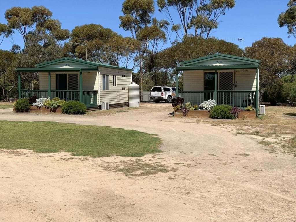 Two small, cream-coloured cabins with green trim sit side by side at Cummins Park and Cabin Park, ea